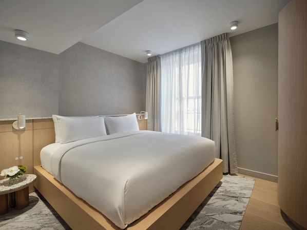 A modern hotel room with a large bed, a bedside table with a lamp, and a view of the outside through sheer curtains. - Corner Apartments (Montréal)