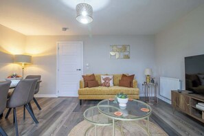 A living room with a sofa, a glass coffee table, a dining area with chairs, a television, and a lamp.