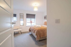 A bedroom with a bed, a chair, a window with blinds, a bedside table, and a wall-mounted light fixture. - Lendrick House - 3 bed house with parking, Falkirk (Falkirk)