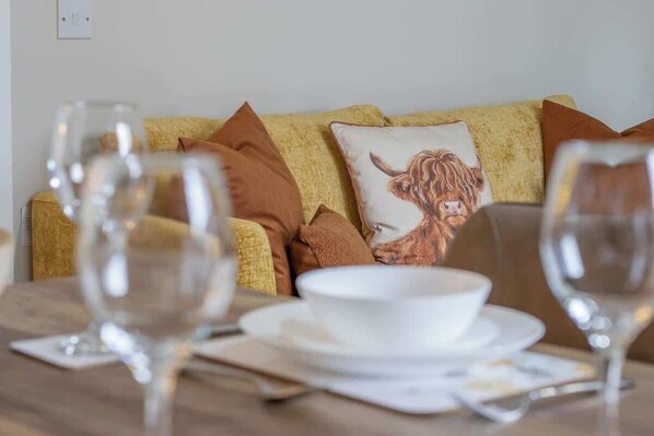 Un comedor con una mesa dispuesta para dos, un sofá con un cojín decorativo y un enchufe de pared.