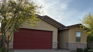 A residential house with a red garage door, a stone foundation, and a clear sky. - Sunlit 4-bedroom West Phoenix Home, Mountain Views & Close to West Gate (Tolleson)