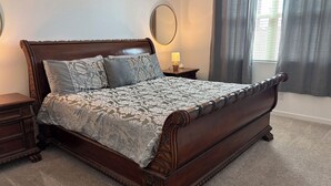 A bedroom with a large bed, a nightstand, a round mirror, and a window with curtains. - Sunlit 4-bedroom West Phoenix Home, Mountain Views & Close to West Gate (Tolleson)