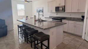 A modern kitchen with white cabinets, a granite countertop, a built-in microwave, and a ceiling fan. - Sunlit 4-bedroom West Phoenix Home, Mountain Views & Close to West Gate (Tolleson)