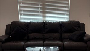 A sectional sofa with a matching ottoman in a room with a large window and tiled floor. - Sunlit 4-bedroom West Phoenix Home, Mountain Views & Close to West Gate (Tolleson)
