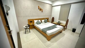 Habitación de hotel con cama de madera, mesita de noche con lámpara, una silla y un escritorio con otra silla.