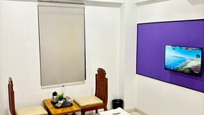 Habitación de hotel con una cama, un escritorio, dos sillas, un televisor montado en la pared y un ventilador de techo.