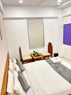 A hotel room with a bed, two chairs, a small table with a plant, and a TV screen. - Pearl Retreat Hotel (Surat)