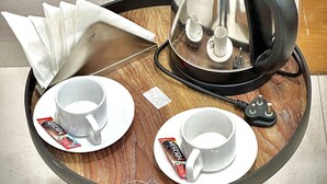 Una pequeña mesa redonda con una cafetera Nescafe, dos tazas blancas y un porta servilletas.