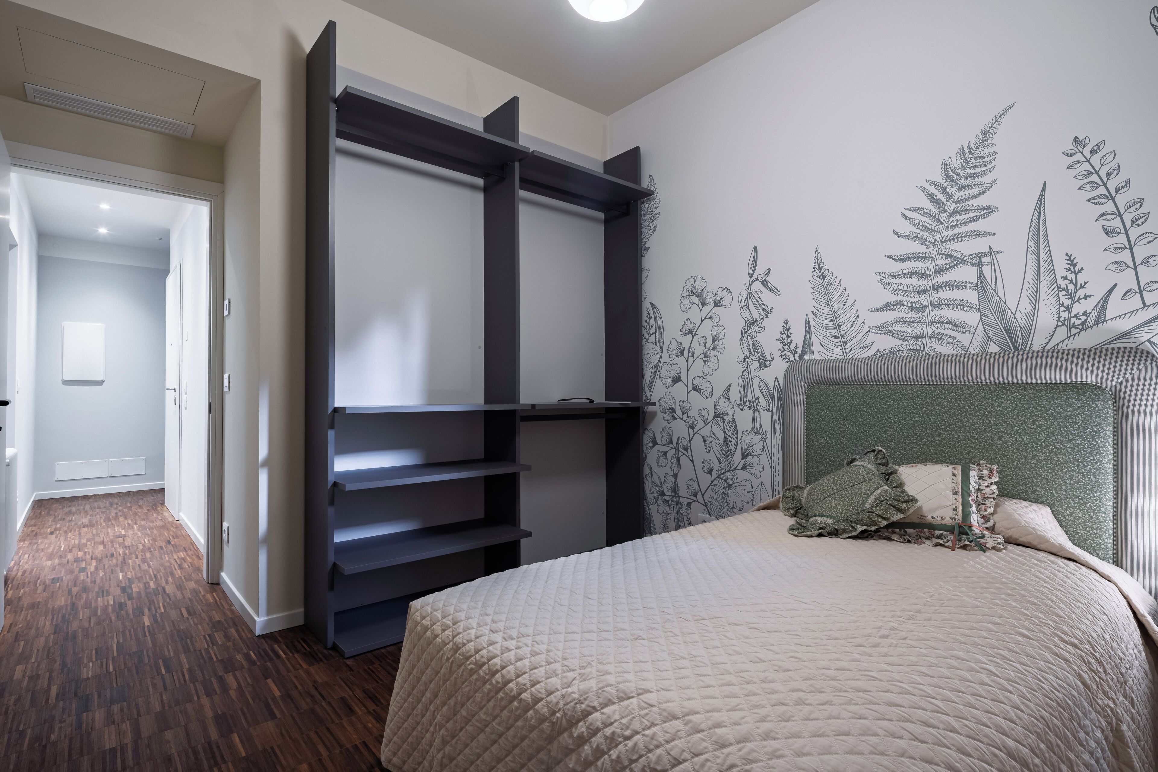 A bedroom with a bed, a wardrobe, and a wall with a botanical mural.