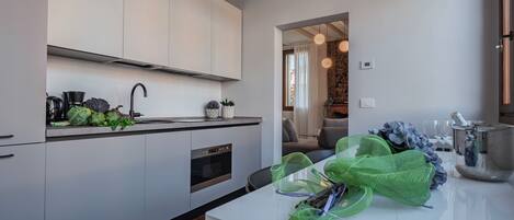 A modern kitchen with white cabinets, a stainless steel oven, and a dining area with a white table and chairs.