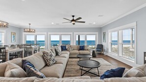 A spacious living room with a large sofa, a dining area, and a view of the ocean. - Honeydew: Beautiful Beachfront Home with Private Pool and Pets Welcome! (Mexico Beach)