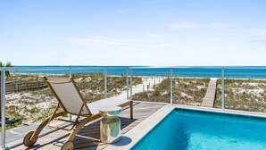 A poolside area with a wooden deck, a lounge chair, and a clear view of the beach and ocean. - Honeydew: Beautiful Beachfront Home with Private Pool and Pets Welcome! (Mexico Beach)