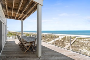 Una terraza de madera con una mesa y sillas, con vista a una playa y al océano.