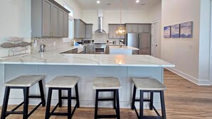 A modern kitchen with a large island, bar stools, and pendant lighting. - Sugarcane: New Construction, Private Pool, 6 Bedrooms (Mexico Beach)
