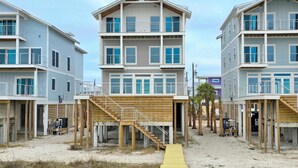 A beachfront property with multiple-story buildings, wooden decks, and a sandy walkway. - Sugarcane: New Construction, Private Pool, 6 Bedrooms (Mexico Beach)