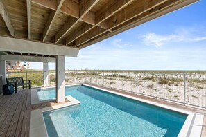 A pool area with a wooden deck, a bench, and a view of the beach.