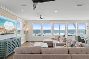 A living room with a large TV, a sofa, and a view of the beach.