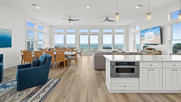 Amplia sala de estar con comedor, cocina con muebles blancos y un ventanal grande con vista al océano.