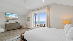 Un dormitorio con una cama grande, vistas a la playa, un ventilador de techo y un escritorio con una silla.