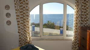 A room with a bed, a window with a view of the sea, and decorative wall art. - "Ocean View Terrace", The best sea view - directly on the beach of Carvoeiro (Carvoeiro)