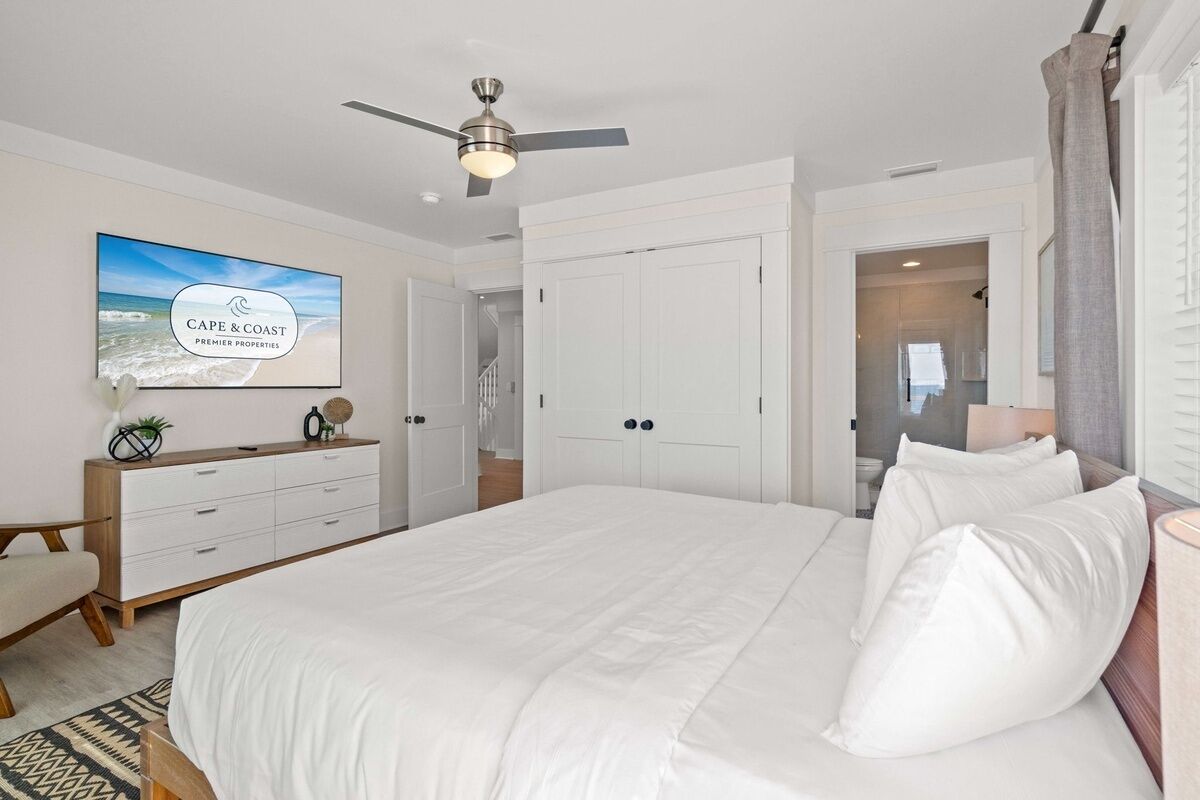 A bedroom with a bed, a ceiling fan, a TV displaying 'Cape & Coast Premier Properties', and a dresser.