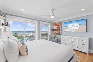 Ein Schlafzimmer mit einem großen Bett, einem Deckenventilator, einem Fernseher und Blick auf den Strand.