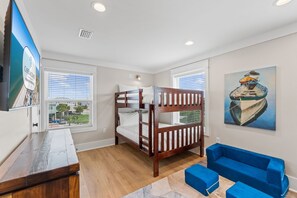 A bedroom with a bunk bed, a desk, a blue sofa, a painting, and a view of the neighborhood. - Paloma: Beachfront in Mexico Beach, Private Pool, Sleeps 24! (Mexico Beach)