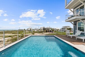 A swimming pool with a wooden deck, a view of houses in the background, and a clear sky. - Paloma: Beachfront in Mexico Beach, Private Pool, Sleeps 24! (Mexico Beach)