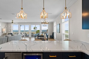 A modern kitchen with a large island, pendant lighting, and a view of the ocean.