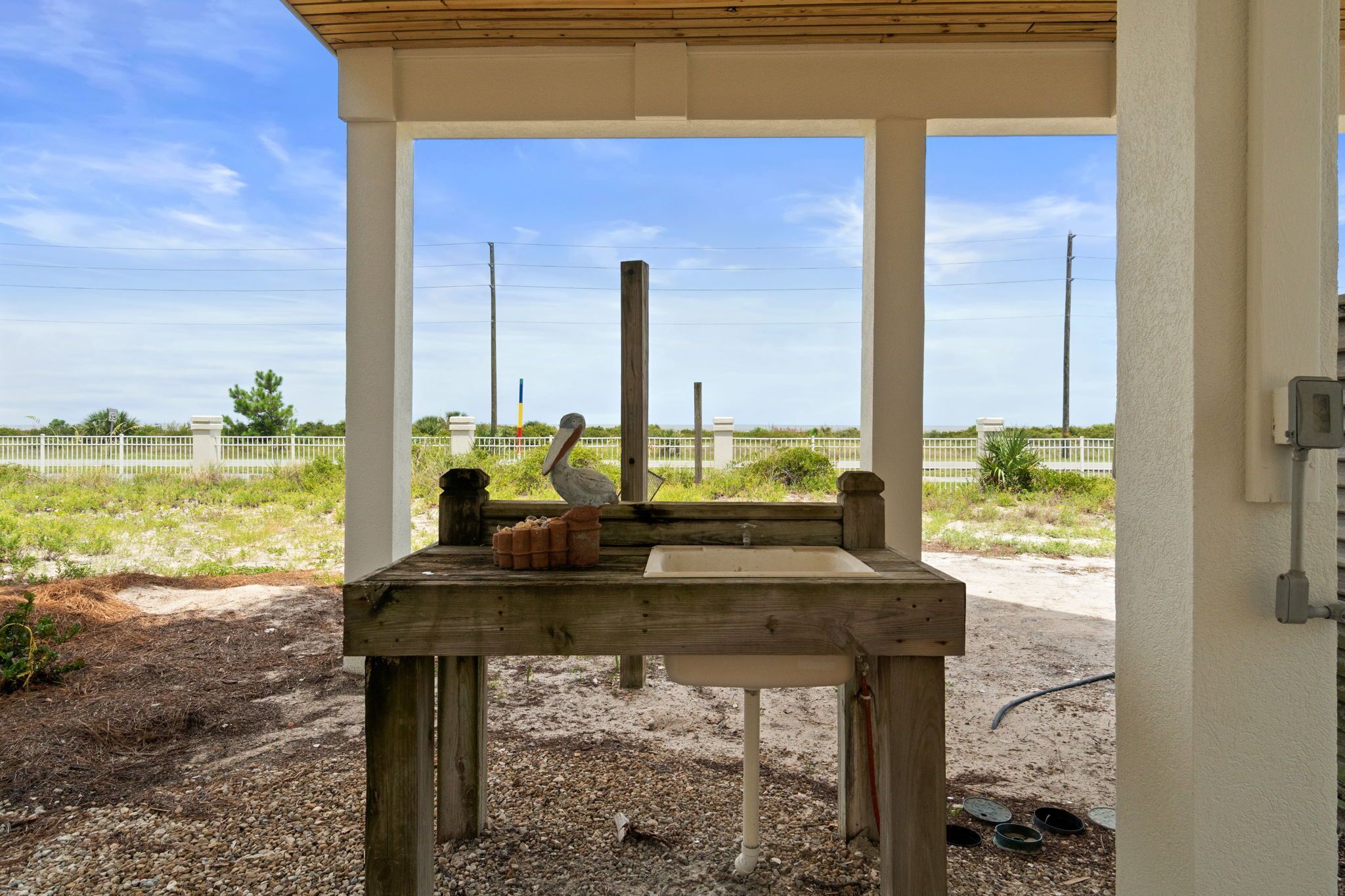 Un espacio al aire libre techado con una mesa de madera, un lavamanos blanco y una escultura de pájaro.