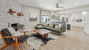 A spacious living room with a brick fireplace, a green sectional sofa, a wooden coffee table, and a cowhide rug.