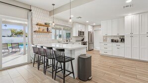 A modern kitchen with white cabinets, a central island, and bar stools.