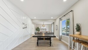 A modern interior with a pool table, wooden flooring, and a view through a large window.