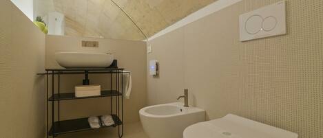 A compact bathroom with a vessel sink, bidet, and toilet.