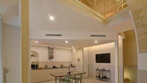 A modern kitchen with a dining area, a TV mounted on the wall, and a staircase leading to an upper level.