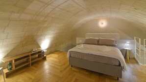 A bedroom with a vaulted ceiling, a bed, a bedside table, and a lamp.