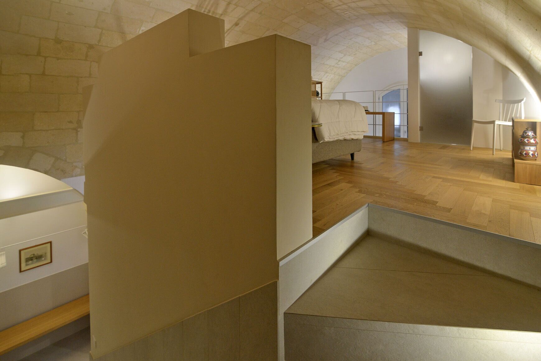 Una habitació àmplia amb un sostre alt, un llit, un paviment de fusta i una paret de pedra.