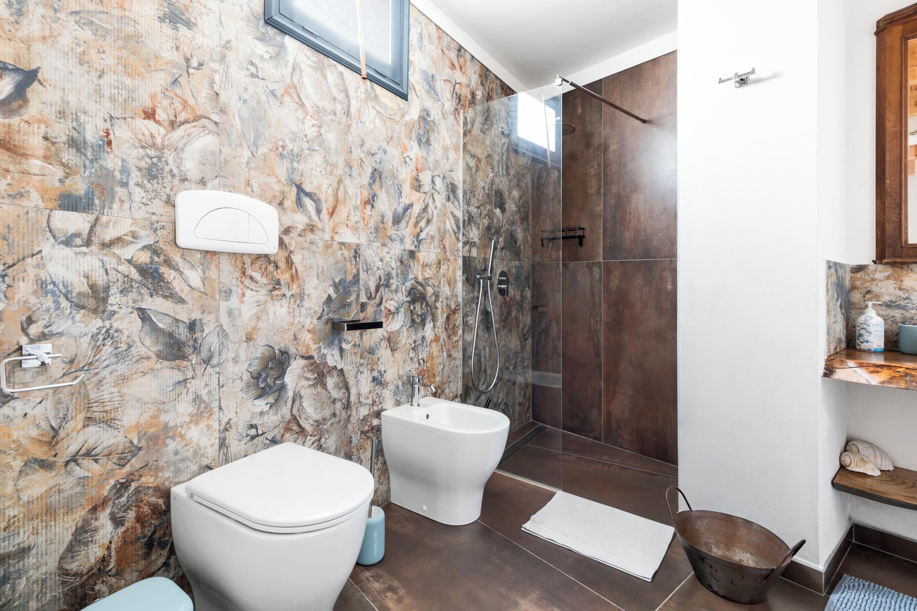 Ein Badezimmer mit Marmorwand, einem Bidet, einer Toilette, einer Duschkabine und einem Ablagebereich für Toilettenartikel.