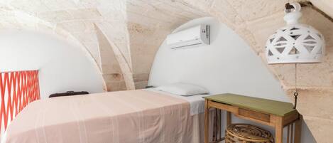 Ein gemütliches Schlafzimmer mit einem Bett, einem kleinen Tisch, einem Korbwannenregal und einer Wand-Klimaanlage.