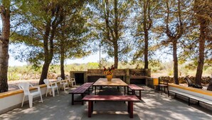 An outdoor dining area with a wooden table and benches, surrounded by trees.