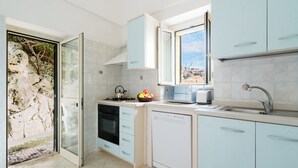 A modern kitchen with light blue cabinets, a dishwasher, a stove, and a window with a city view.