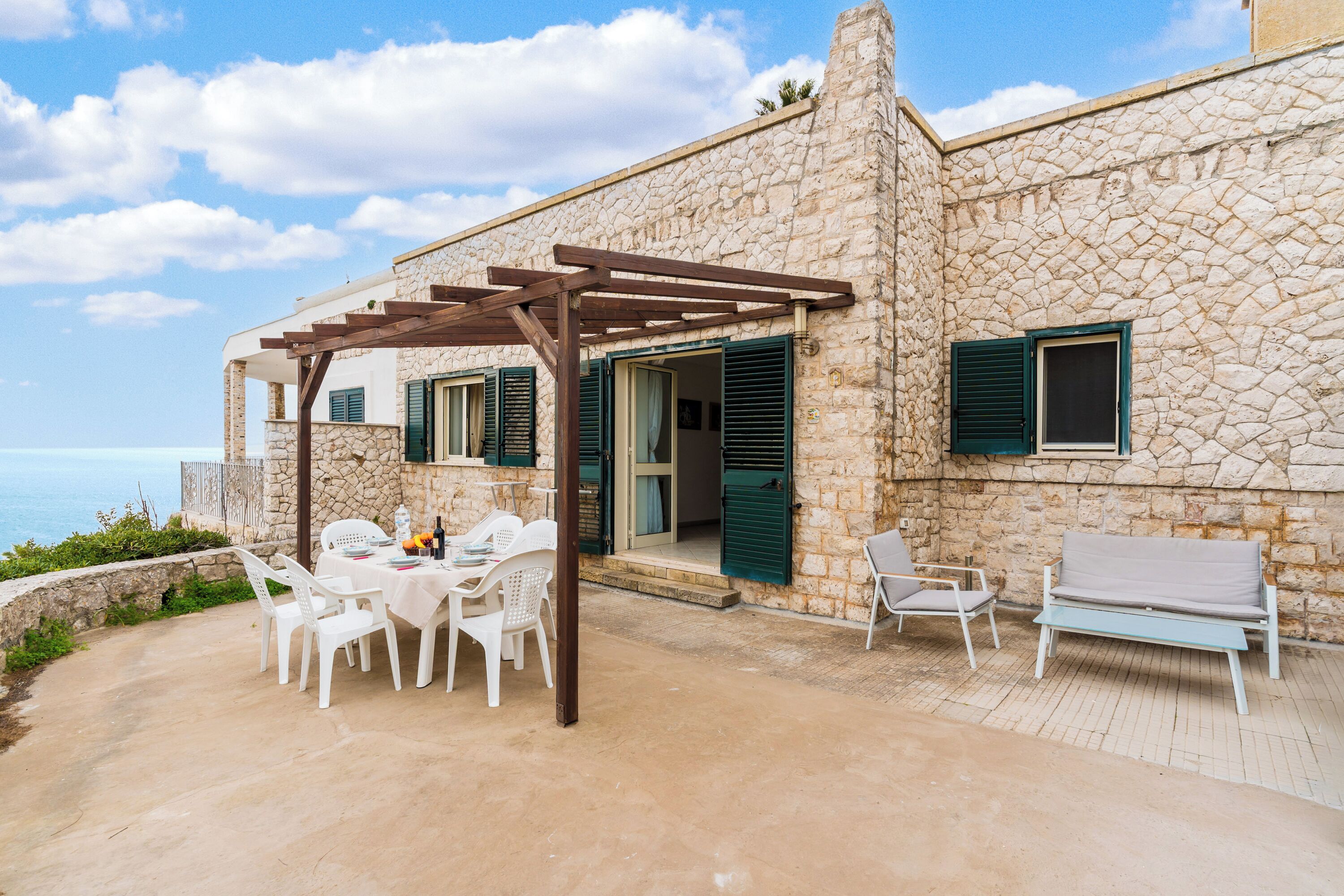 A stone building with a covered patio, outdoor seating, and a view of the sea.