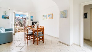 A spacious living room with a dining area, white walls, and a view through an open door.