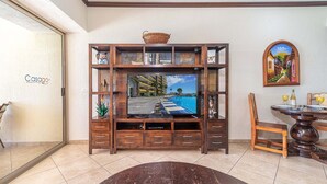 Una sala de estar con televisor, mueble de madera para entretenimiento, mesa de comedor y sillas.