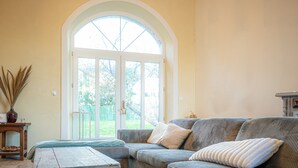 A living room with a large arched window, a sofa, and a small table with decorative items. - Le Florentin - Spacious Family Home in a Peaceful Village near Limoges (Condat-sur-Vienne)