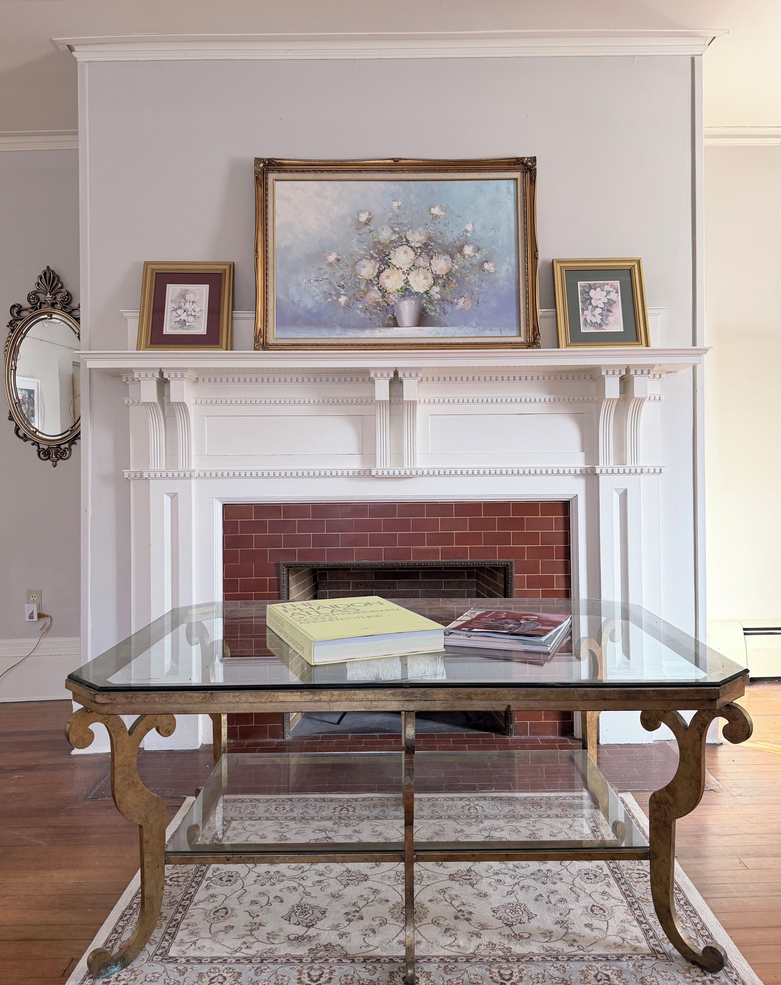 Una habitación con una mesa de vidrio, una chimenea con revestimiento de ladrillo y un cuadro enmarcado encima.