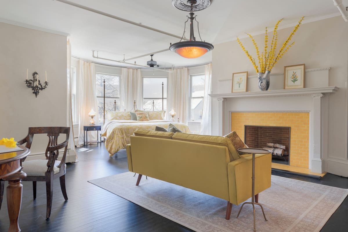 A spacious living room with a yellow sofa, a fireplace, and a dining area with a table and chairs.
