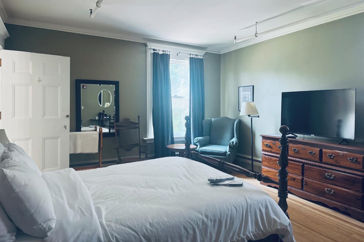 A hotel room with a bed, a chair, a dresser, a television, and a window with curtains.