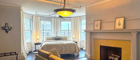 A bedroom with a bed, a sofa, a fireplace, and a chandelier.