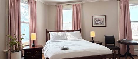 A neatly arranged bedroom with a wooden bed, bedside lamps, a chair, and a small table.
